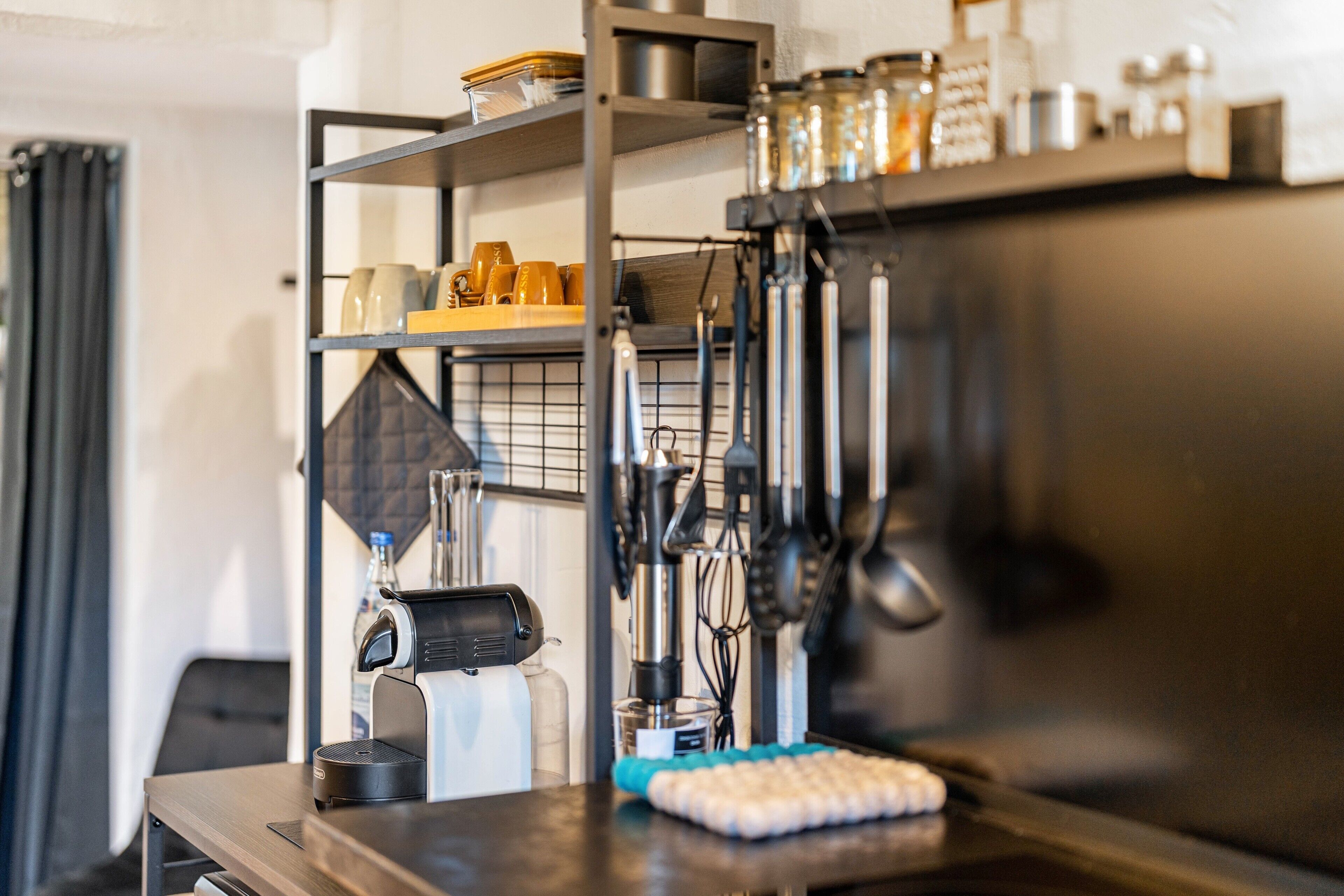 A kitchen area with a coffee machine, utensils, and storage shelves.