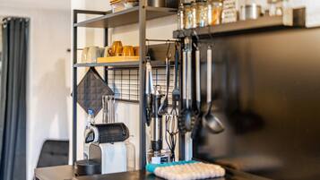Un coin cuisine équipé d’une machine à café, d’ustensiles et d’étagères de rangement.