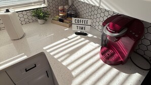 Cozinha com armários brancos, uma cafeteira, um letreiro que diz 'COFFEE TIME' e uma janela com persianas.