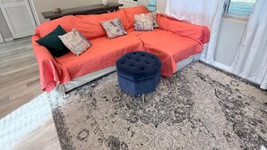 Um quarto com um sofá vermelho, um banquinho azul, um tapete estampado e obras de arte emolduradas na parede.