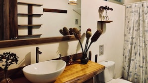 Een badkamer met een houten wastafel, een witte wasbak, een spiegel, een toilet en een douchegordijn met een vismotief.