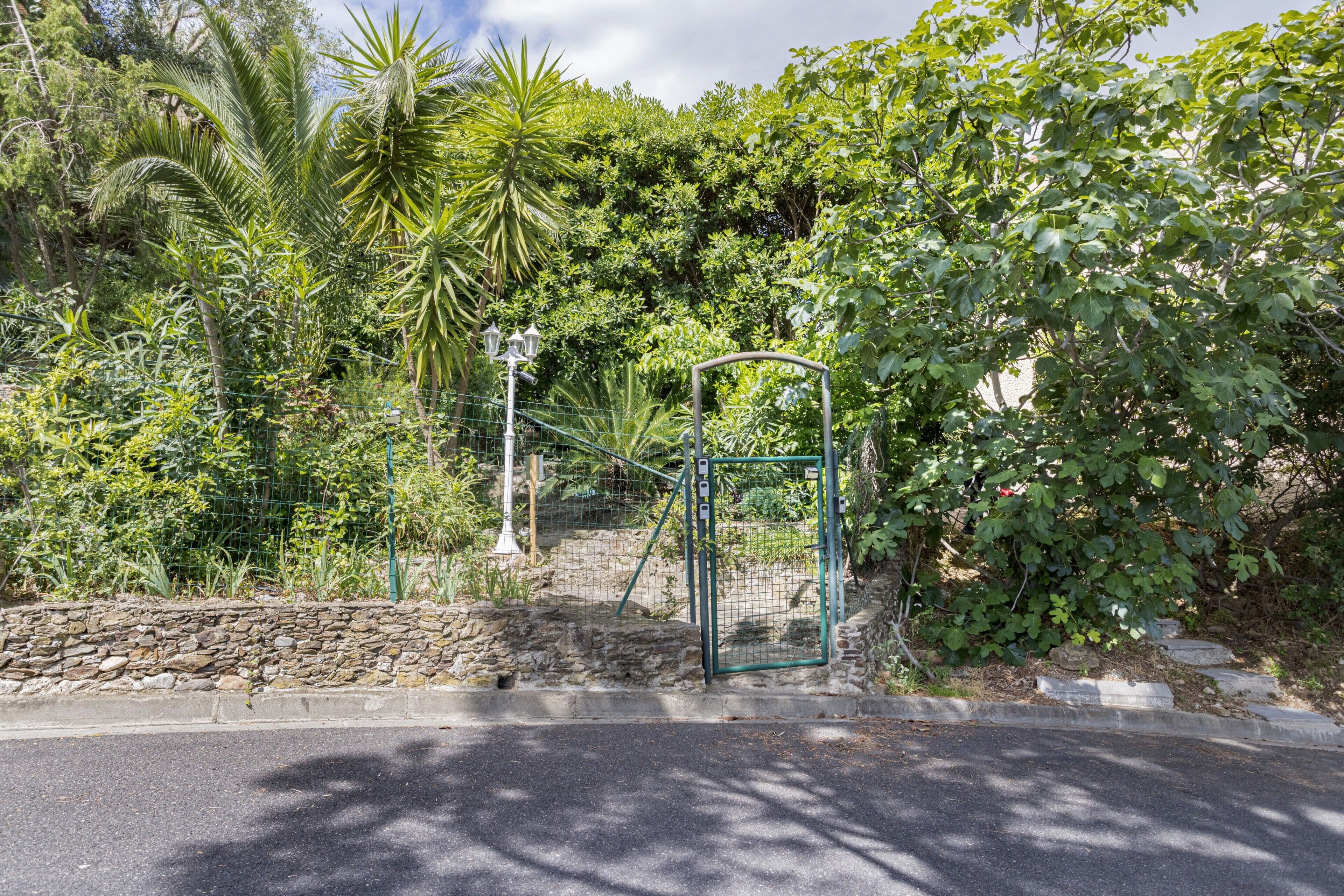 A gated entrance with a stone wall, surrounded by lush greenery and trees.