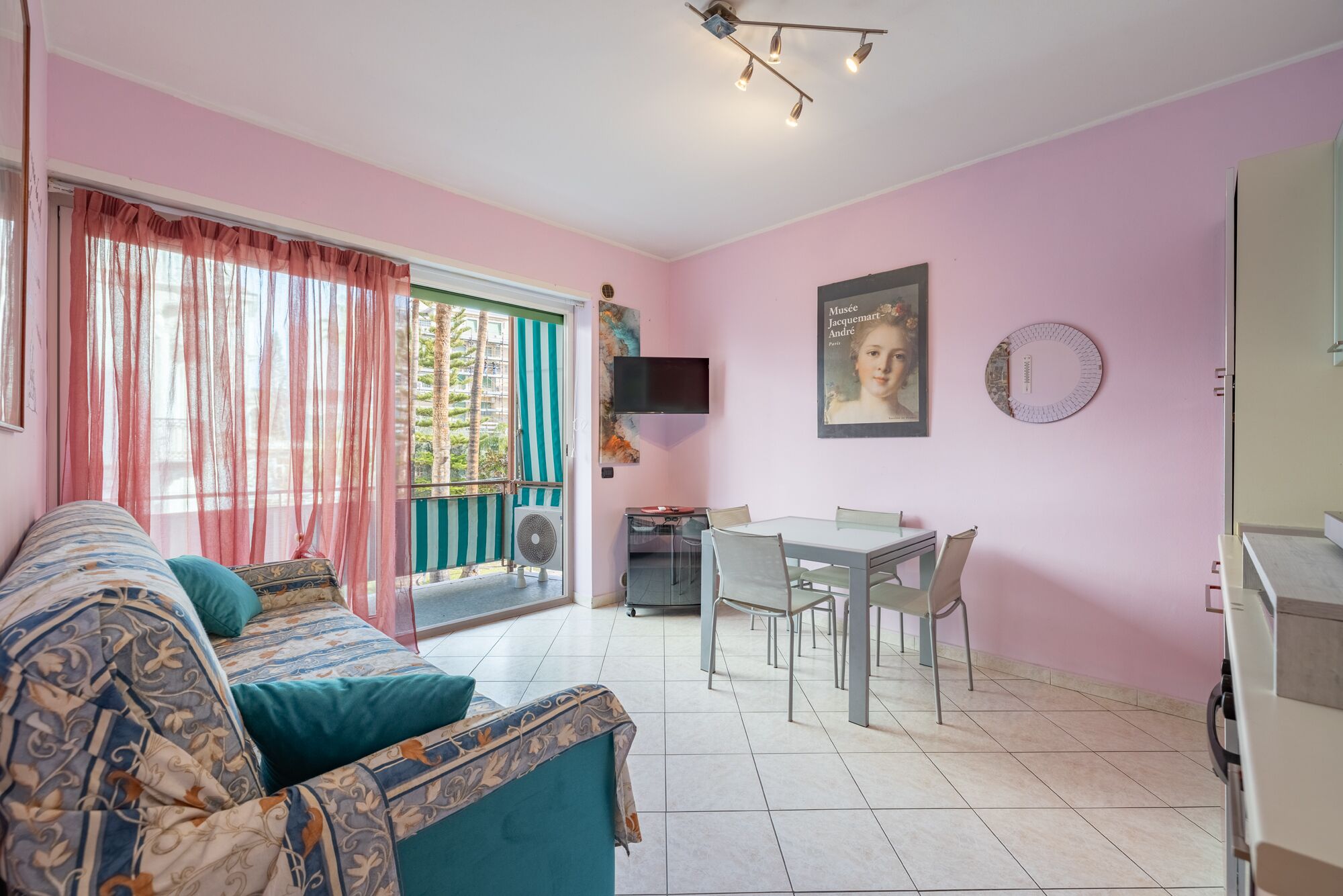 A room with a sofa, a dining table with chairs, a TV, and a window with curtains.