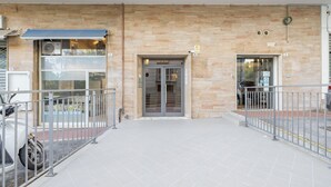 Entrada de un edificio con un área techada, puerta de cristal y valla metálica.