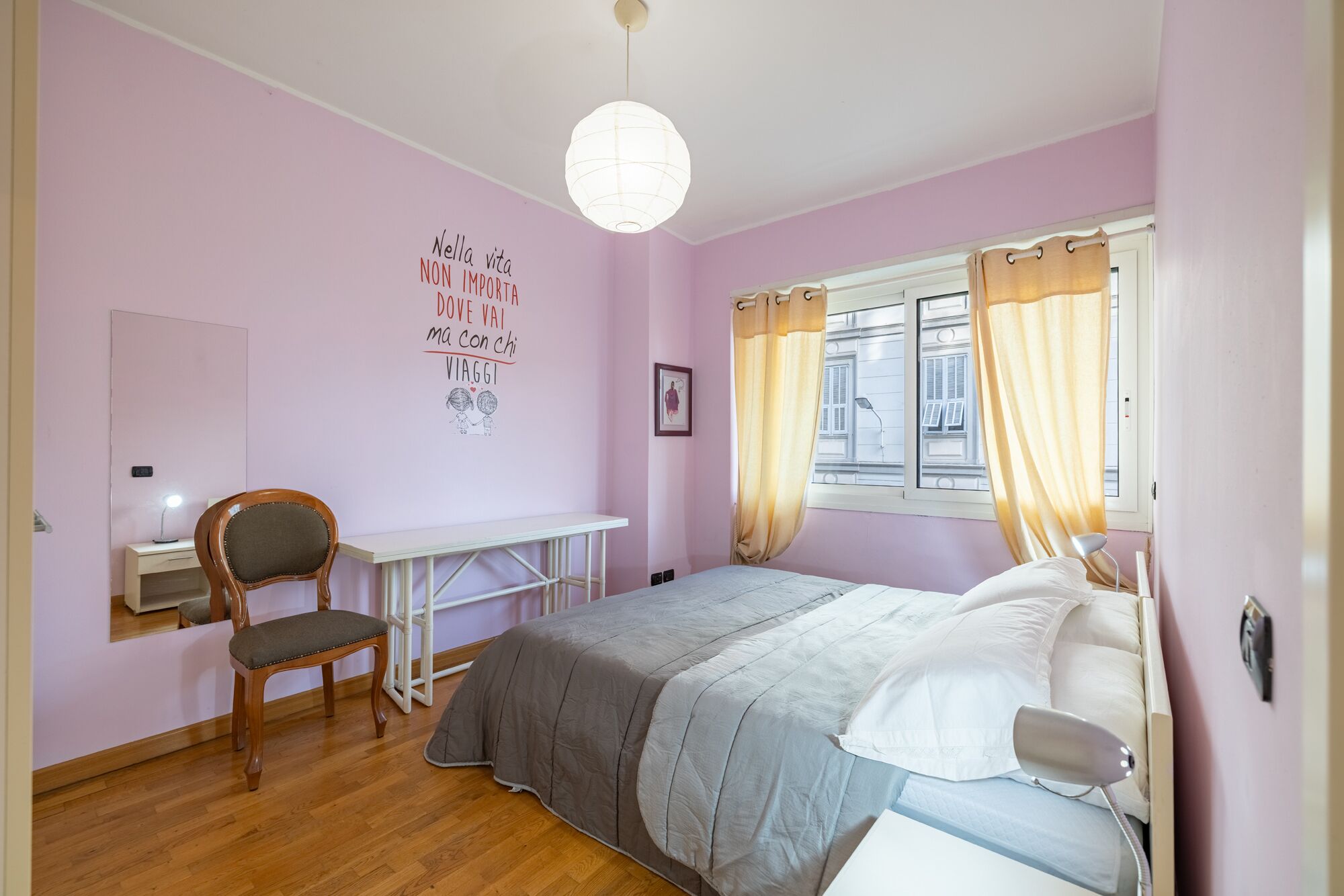 A bedroom with a bed, a desk, a chair, a wall with a motivational quote, and a window with curtains.