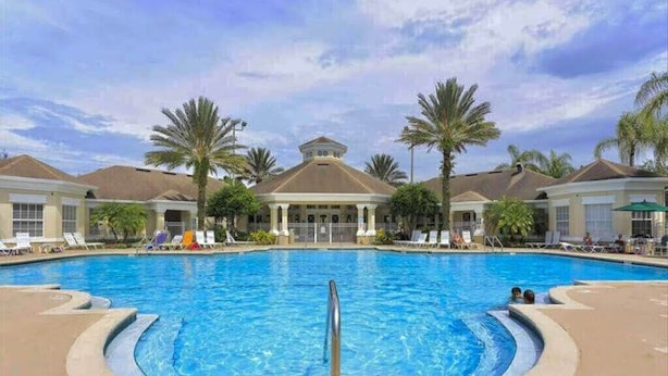 A swimming pool with a central fountain, surrounded by palm trees and lounge chairs.