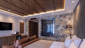 A modern bedroom with a large bed, a seating area, a stone wall, and a TV.