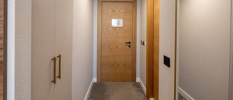 Un couloir étroit avec une porte en bois, un interrupteur et un thermostat fixés au mur.