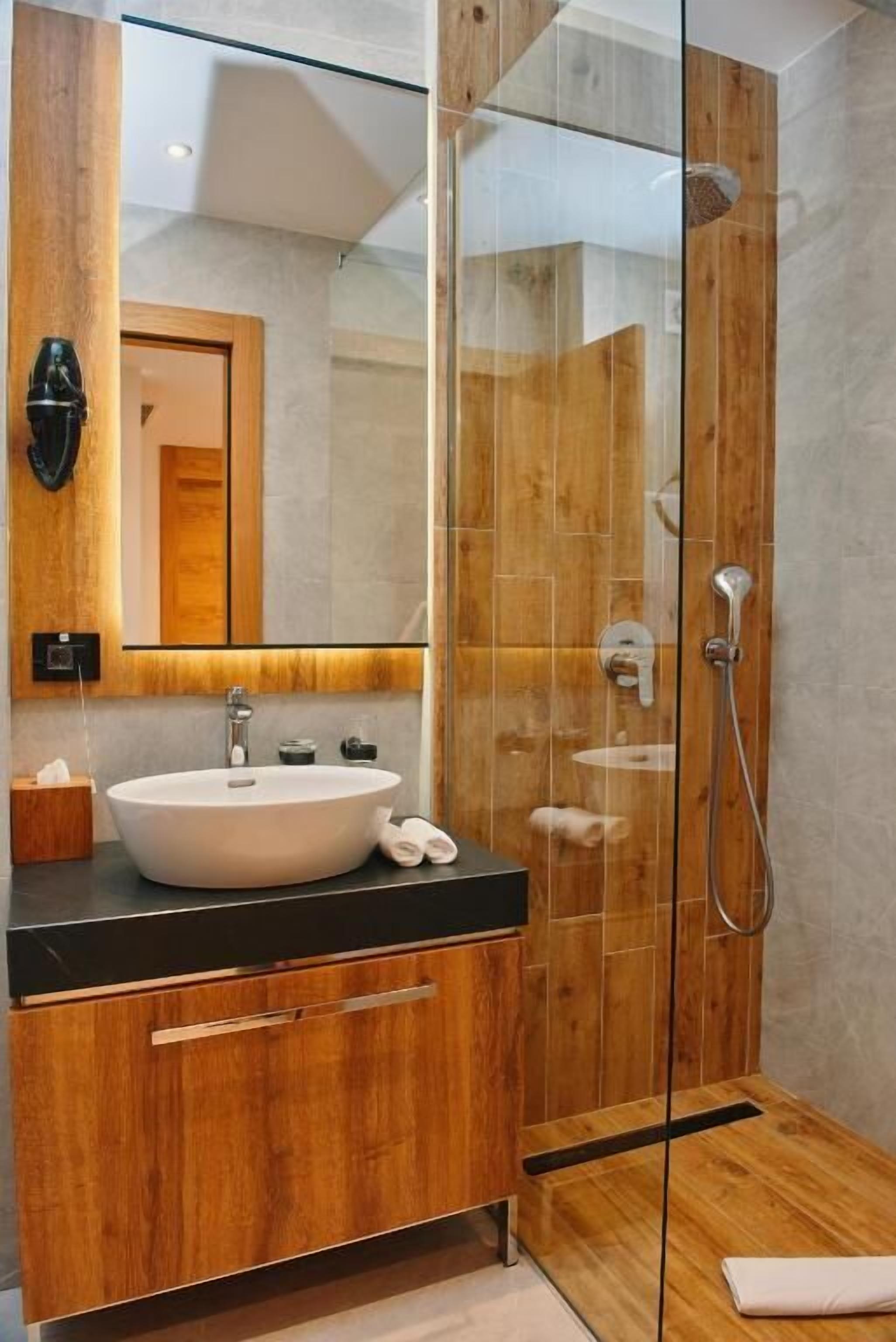 Un baño moderno con ducha envuelta en vidrio, tocador de madera y un espejo grande.