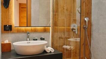 Un baño moderno con ducha envuelta en vidrio, tocador de madera y un espejo grande.