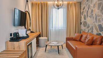A modern hotel room with a wooden desk, a television, a stone wall, a leather sofa, and a round table.