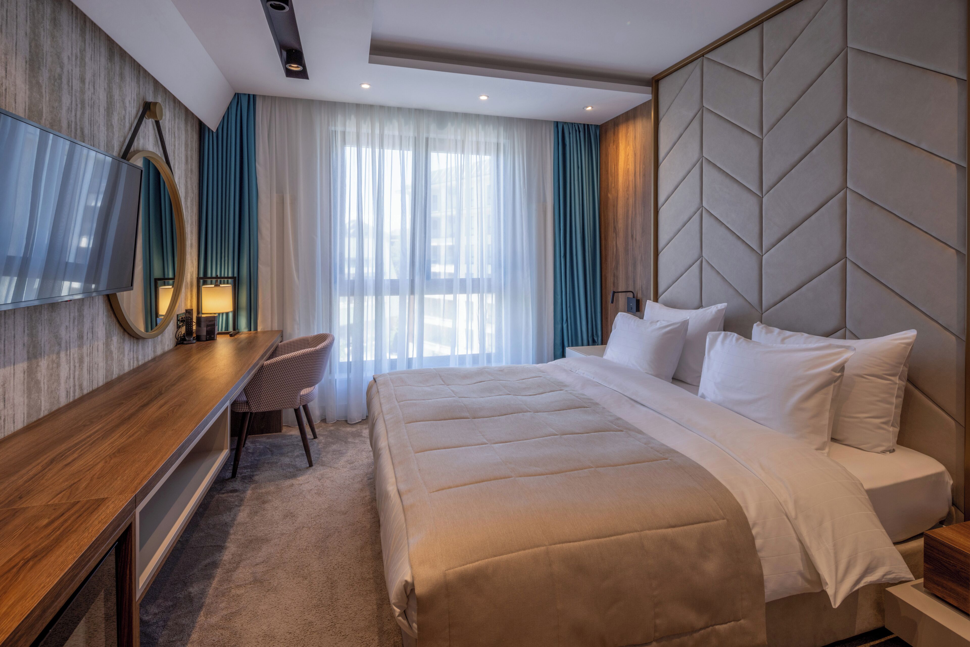 Une chambre d’hôtel avec un lit, un bureau, une chaise, une télévision et une grande fenêtre avec des rideaux.