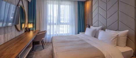 Une chambre d’hôtel avec un lit, un bureau, une chaise, une télévision et une grande fenêtre avec des rideaux.