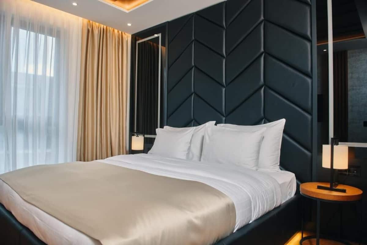 Une chambre d’hôtel moderne avec un grand lit, un mur à la texture sombre et une table de chevet avec une lampe.