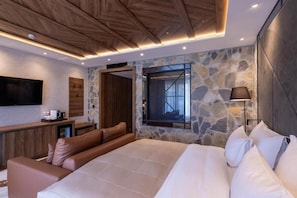 A modern bedroom with a large bed, a wooden ceiling, stone walls, a stone fireplace, and a flat-screen TV. - Hotel Zlatibor (Zlatibor)