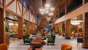 A spacious lobby with high ceilings, wooden paneling, and a central seating area with tables and chairs.