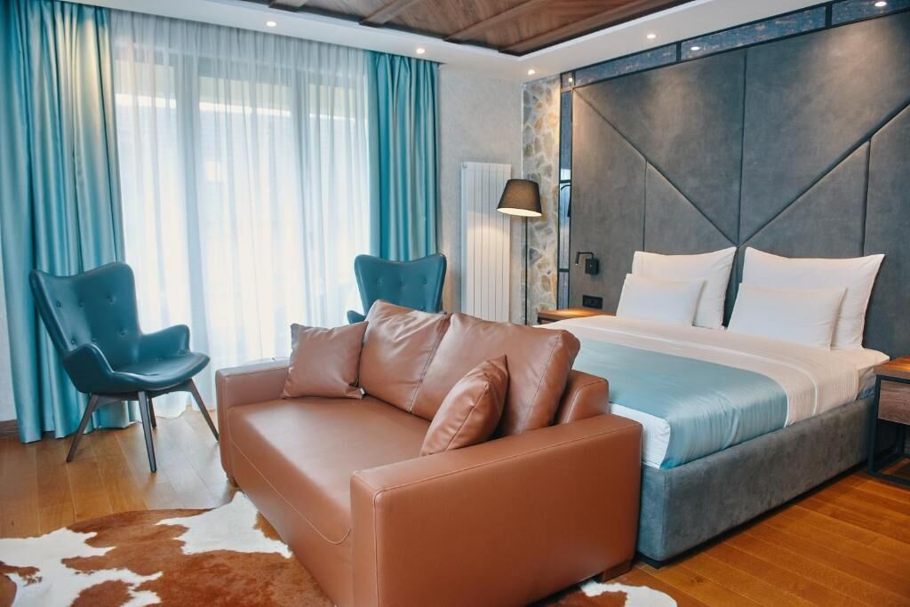 A modern hotel room with a large bed, a sofa, a chair, and a stone accent wall.
