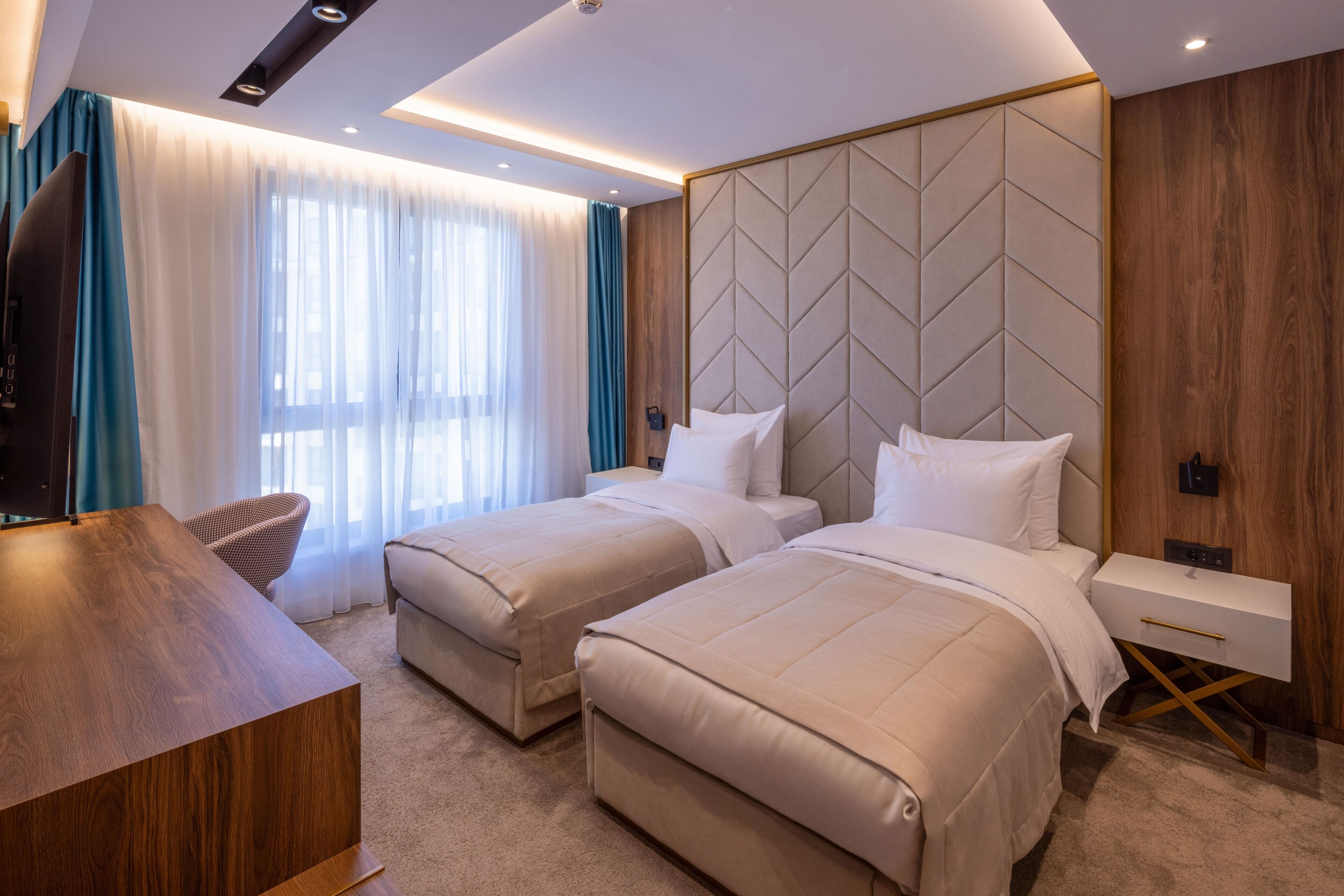 Habitación de hotel con dos camas, un escritorio, un televisor y un panel decorativo de madera.