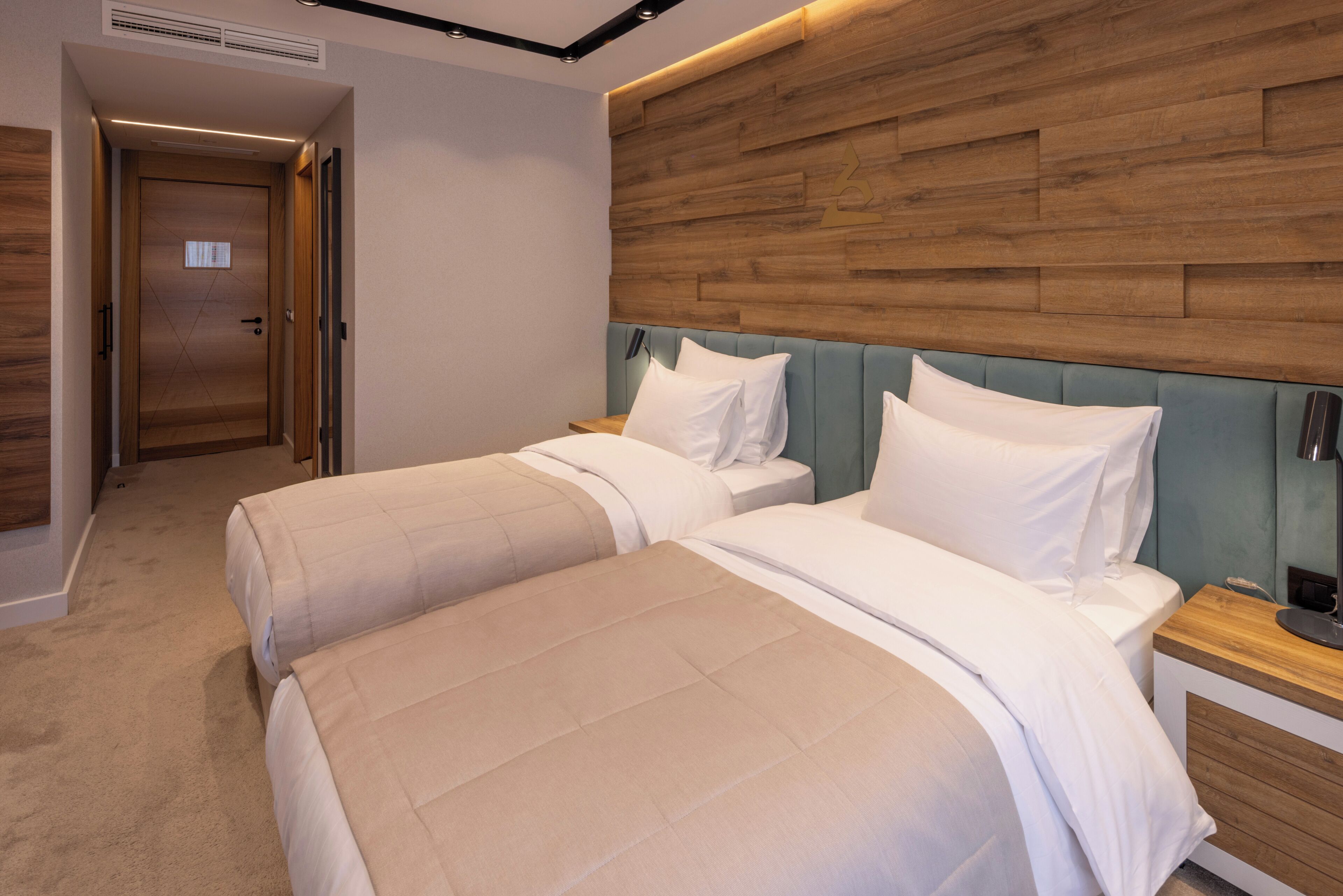 A hotel room with two beds, a wooden headboard, a bedside table, and a carpeted floor.