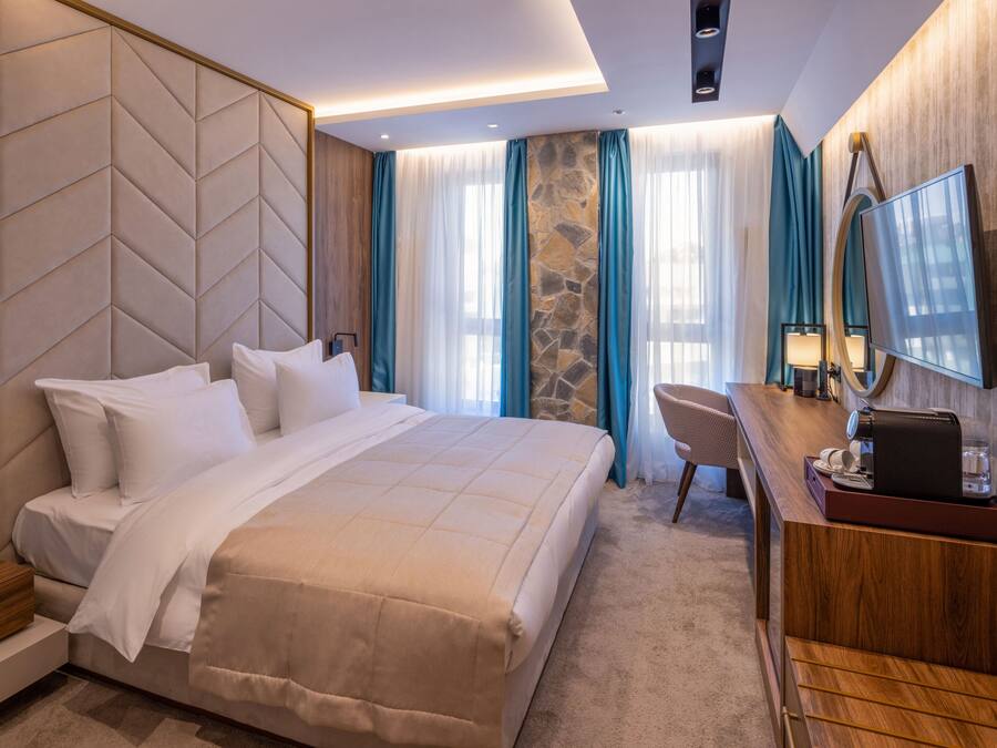A hotel room with a bed, a desk, a chair, a TV, and a stone accent wall.
