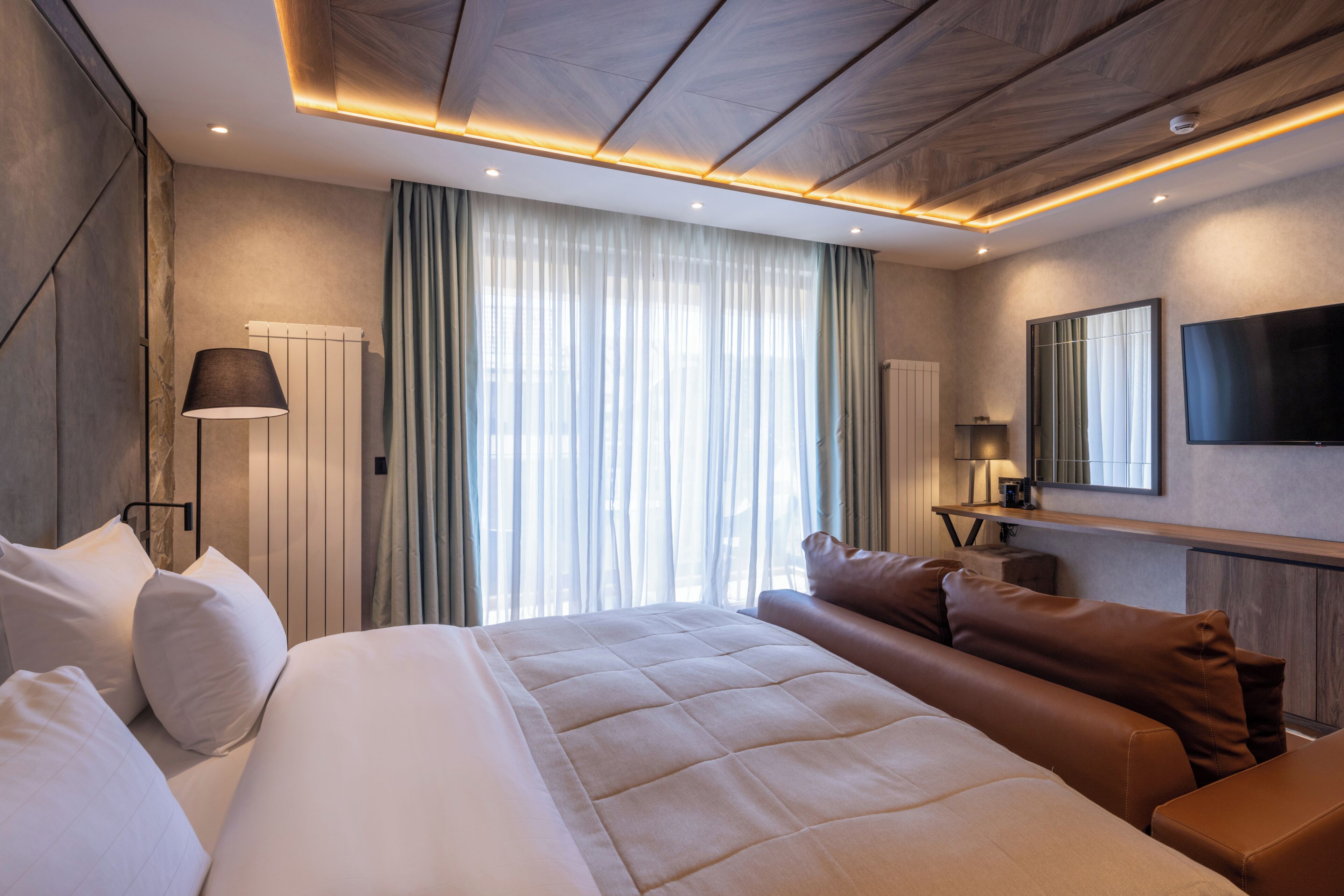 Une chambre d’hôtel moderne dotée d’un grand lit, d’un coin salon, d’une télévision à écran plat et d’une fenêtre avec des rideaux.