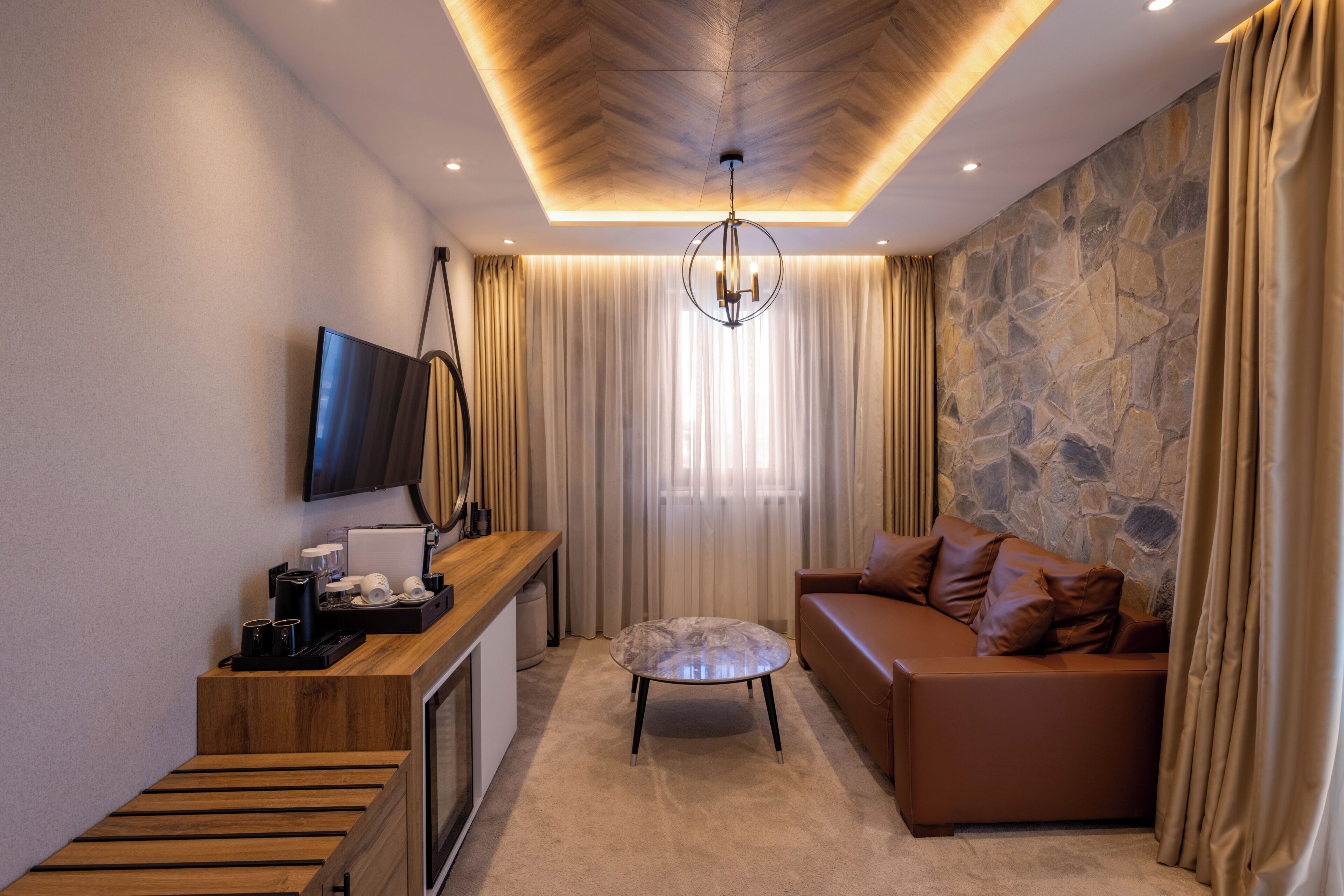A modern living room with a stone wall, a wooden bench, a sofa, a television, and a chandelier.