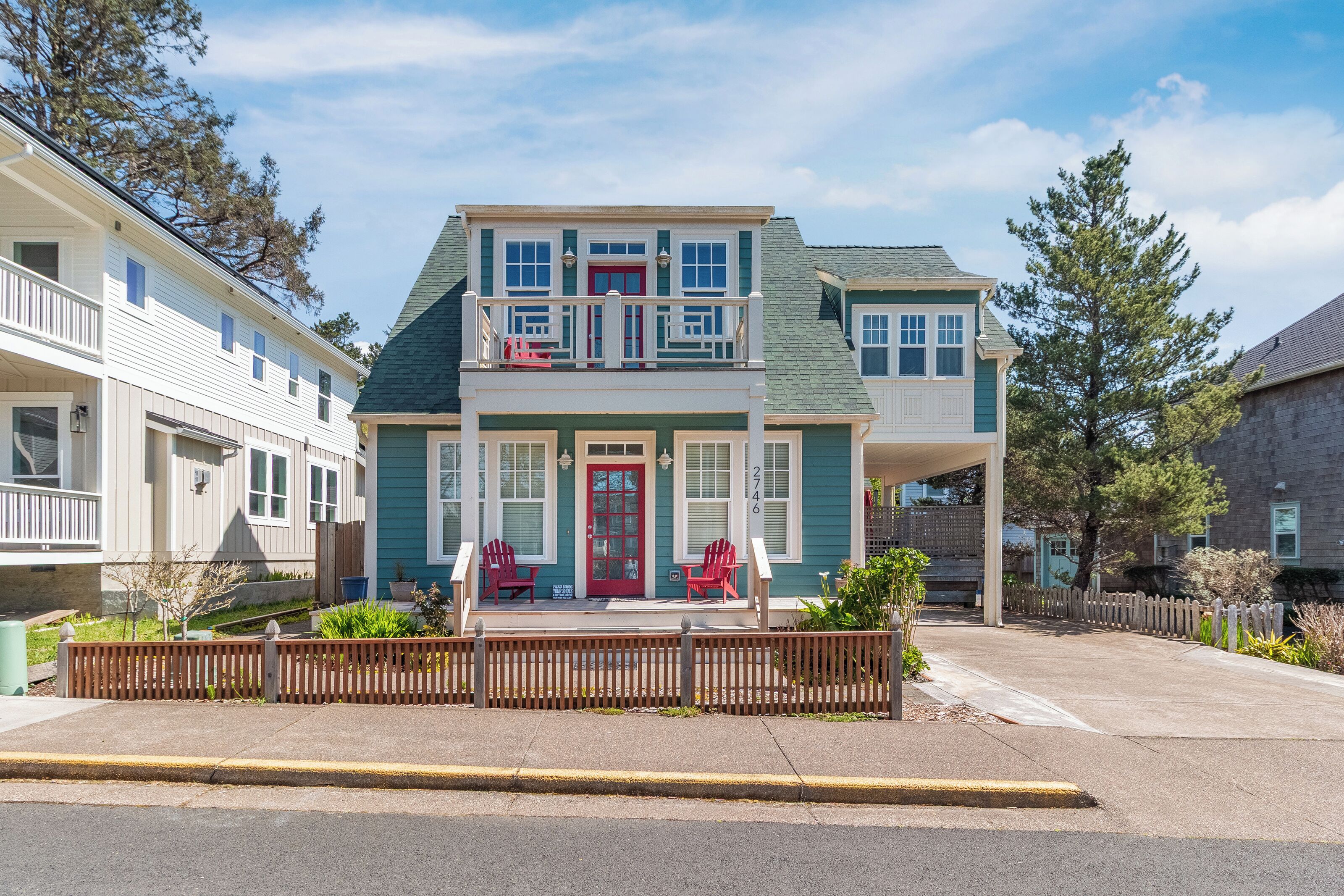 Charming coastal cottage with teal siding, red door, and welcoming front porch in peaceful neighborhood setting.