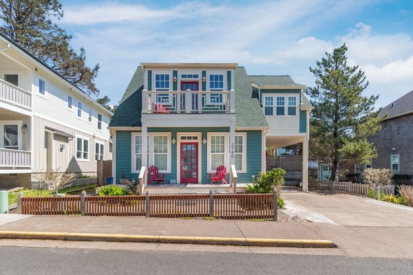 Charming coastal cottage with teal siding, red door, and welcoming front porch in peaceful neighborhood setting.