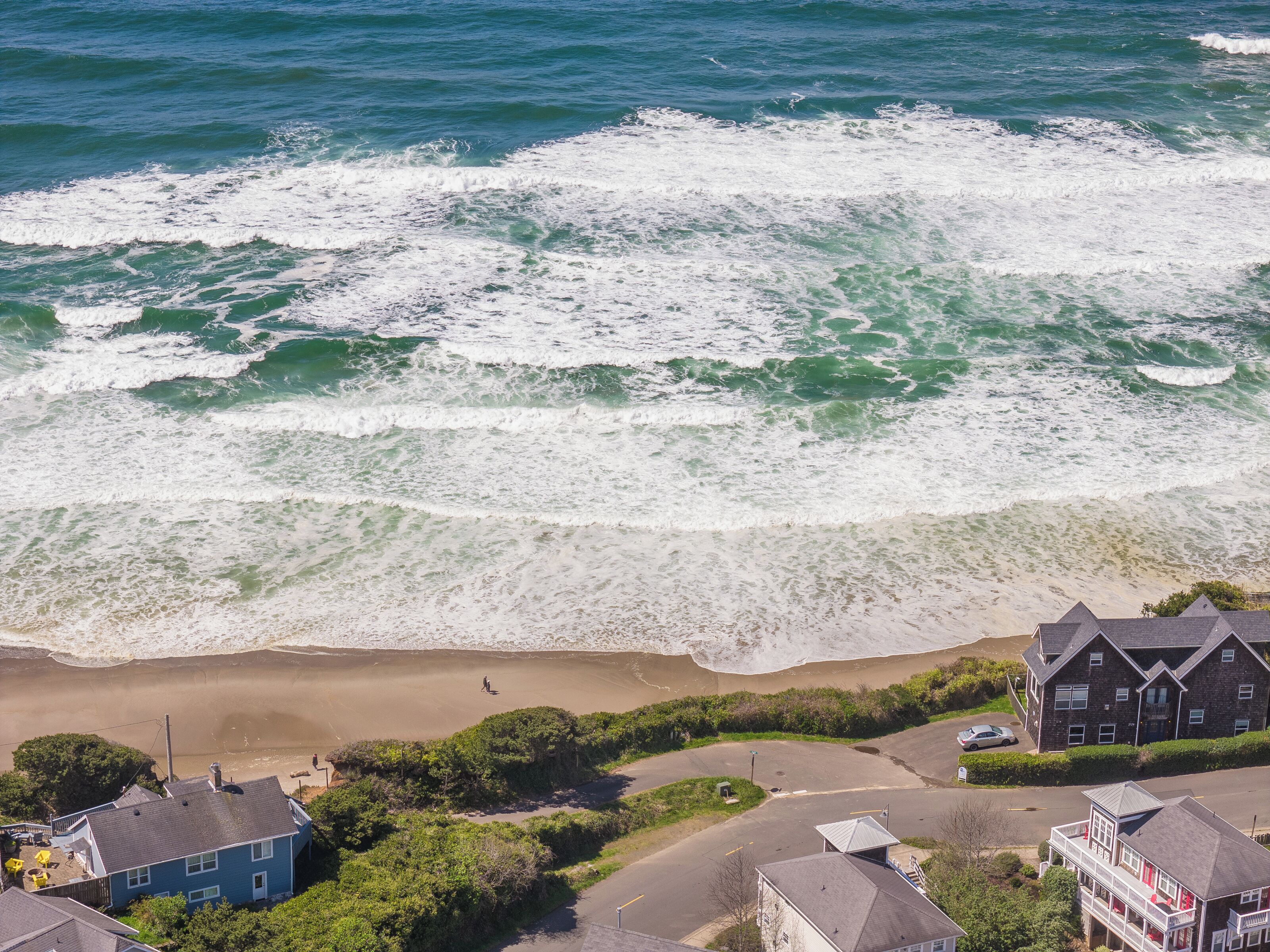 Aerial view of oceanfront properties nestled between pristine beach and rolling waves, showcasing the coastal community's prime location.