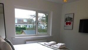 Een slaapkamer met een bed, een raam, een radiator, een aan de muur bevestigde televisie en een poster.