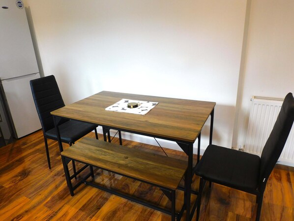 A small dining area with a wooden table and four black chairs, one bench, and a white radiator in the background.