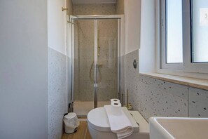 Een badkamer met een douchecabine, een toilet, een bidet en een raam boven de wastafel.