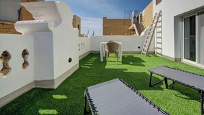 En tagterrasse med græstæppe, et bord, en stol og en stige.