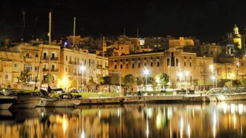 Une vue nocturne d’une ville, avec ses bâtiments, un pont et une étendue d’eau calme qui reflète les lumières.