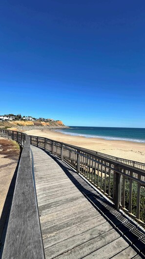Une promenade en bois qui mène à une plage, avec un ciel bleu et dégagé.