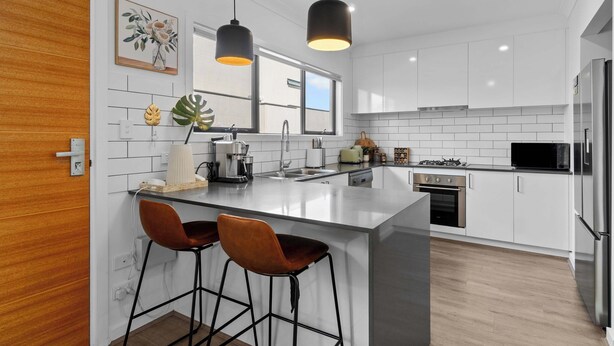 A modern kitchen with white cabinets, a central island, two bar stools, pendant lighting, and a large window.
