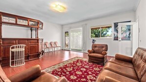 Un vaste salon doté d’un bar en bois, de canapés en cuir, d’un tapis rouge à motifs et d’une grande fenêtre offrant une vue sur la verdure.