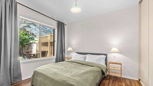 Une chambre à coucher avec un lit, deux lampes de chevet, une fenêtre avec des rideaux et un plancher en bois.