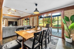 A spacious dining area with a wooden table and chairs, a sofa, and a television in the background.