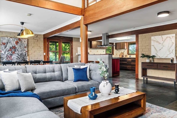 A spacious living room with a grey sectional sofa, a wooden coffee table, and a dining area in the background.