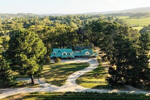 A large, single-story building with a green roof, surrounded by lush greenery and a winding path.