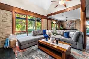 A spacious living room with a sectional sofa, a coffee table, and large windows offering a view of greenery.