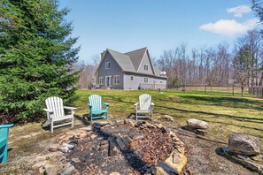 Ein Haus mit Feuerstelle und Adirondack-Stühlen im Garten.