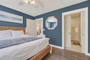 Un dormitorio con una cama, un ventilador de techo, un espejo grande y una puerta que da a otra habitación.