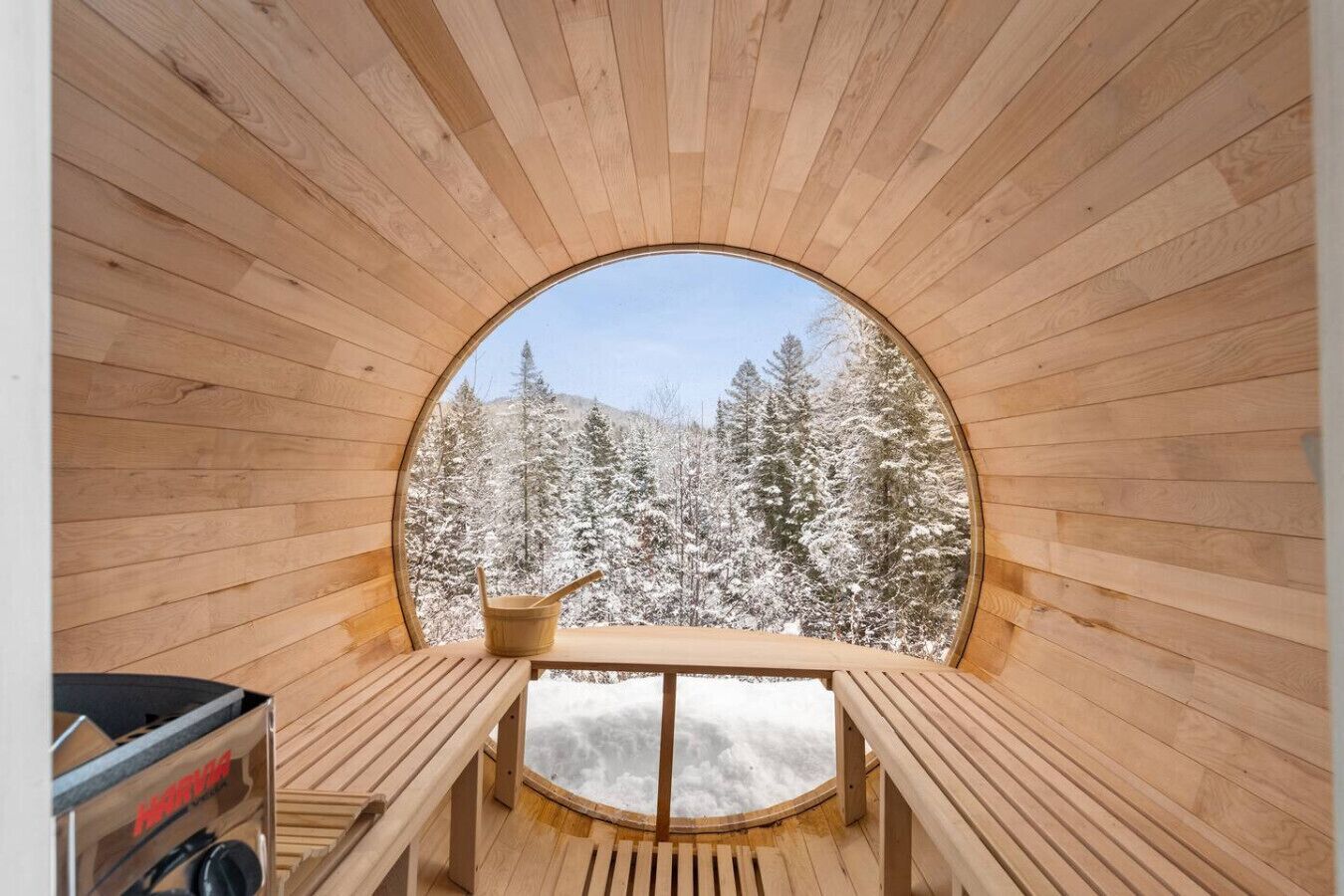 Une cabane en bois avec une fenêtre ronde, un banc en bois et un seau en bois.