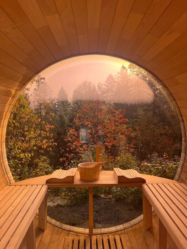 Une pièce circulaire en bois, avec un banc et une table, d’où l’on peut admirer les arbres et le feuillage à l’extérieur.