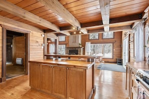 A spacious kitchen with wooden cabinets, a large island, and a stone fireplace.