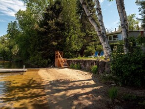 A lakeside property with a wooden staircase leading to a dock, surrounded by dense trees and a stone wall. - Le Kaïa, Bord de L`eau, Plage, spa et foyer (Nominingue)