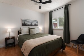 A bedroom with a bed, two bedside lamps, a ceiling fan, a window with curtains, and a chair. - Le Kaïa, Bord de L`eau, Plage, spa et foyer (Nominingue)