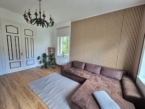 Ein Wohnzimmer mit braunem Sofa, einer Wand mit Muster, einer Chandelier und Holzboden.